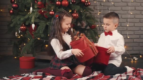 Маленькі діти тримають подарунки біля ялинки — стокове відео