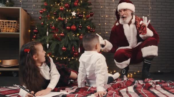 Santa claus sitting quietly near xmas tree and going to make surprise for kids — Stock Video