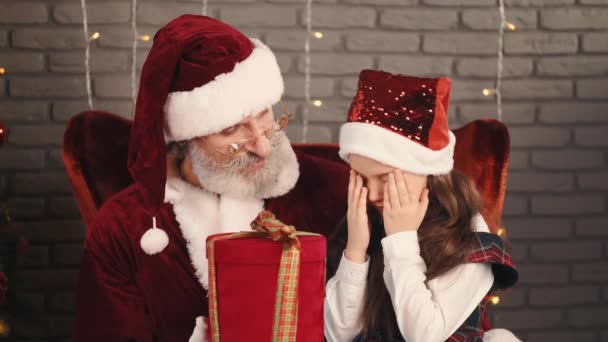 サンタは赤い箱の中で贈り物を提示する彼と一緒に座っている女の子に — ストック動画