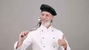 Şapka ve ekipman giymiş profesyonel bir şef elinde kepçeyle ayakta duruyor ve gülümsüyor.