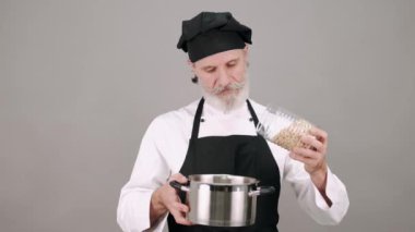 Orta yaşlı aşçı gri arka plana mısır gevreği döküyor.