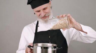 Orta yaşlı aşçı gri arka plana mısır gevreği döküyor.