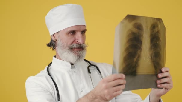 Médico sênior masculino olhando para a imagem de raios-x no fundo amarelo — Vídeo de Stock