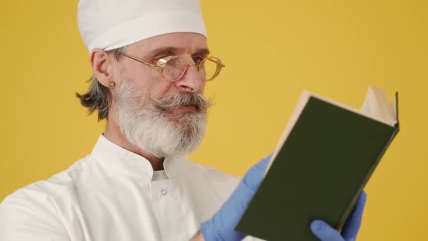 Médico sênior com um livro sobre fundo amarelo — Vídeo de Stock