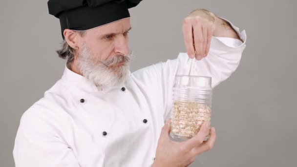 Chef de meia idade homem derramando cereais em fundo cinza — Vídeo de Stock