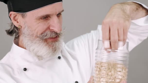 Chef de meia idade homem derramando cereais em fundo cinza — Vídeo de Stock