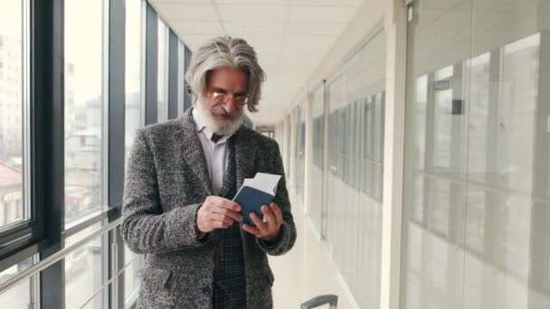 Elegant senior man checking passport and bording pass at corridor in the airport — Stock Video