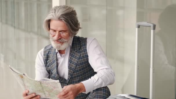 Senior man planning vacation with a map sitting at the airport — Stock Video