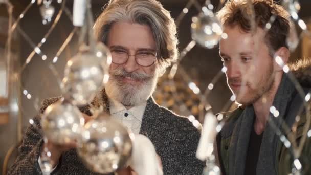 Glada män tittar på julbollar och ljus i butiken — Stockvideo