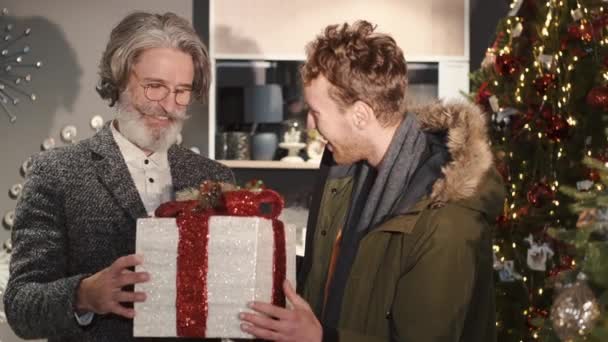 Viejo y elegante hombre desempacando un regalo con su nieto en una habitación decorada para Navidad — Vídeo de stock