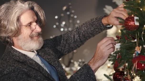 Stijlvolle oude man versieren kerstboom thuis — Stockvideo