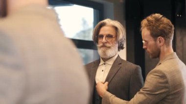 Erkek giyim mağazasında danışman ile takım elbise deneyen bir adam.