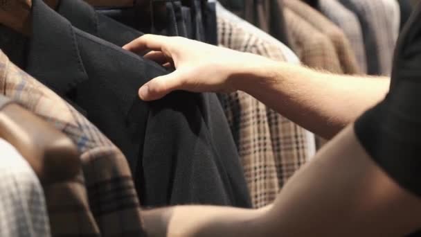 Een man kijkt door multi-gekleurde jassen op een hanger in een winkel — Stockvideo