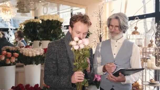 Man och senior florist konsult väljer bukett på blommor butik — Stockvideo