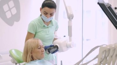 Sandalyedeki hastaya diş röntgeni çeken kadın dişçi ya da teknisyen.