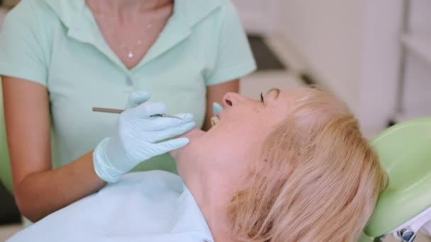 Dentist de sex feminin care examinează dinții femeii în vârstă în birou — Videoclip de stoc
