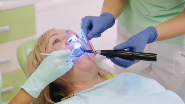 Dentist using ultraviolet lamp on ld womans teeth — Stock Video