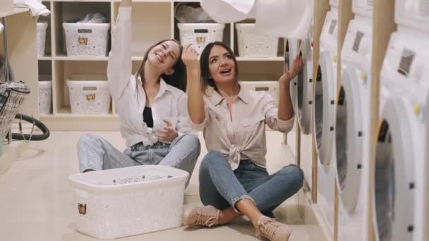 Two happy girlfriends having fun together while washing in the self-service laundry — Stock Video