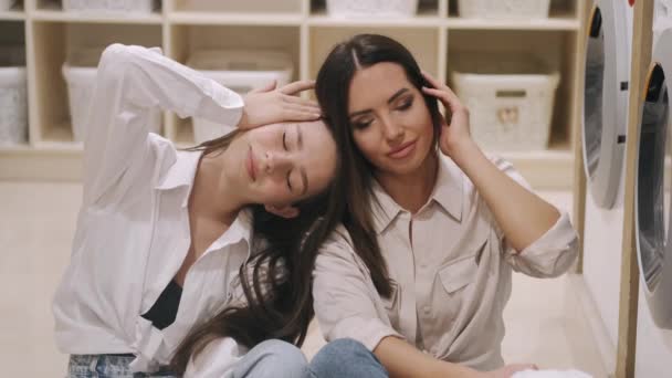 Two happy girlfriends having fun together while washing in the self-service laundry — Stock Video