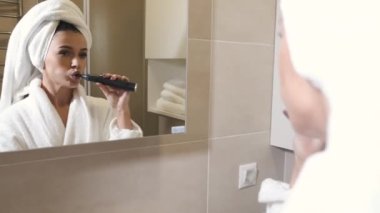 Woman in robe and towel brushing teeth in bathroom
