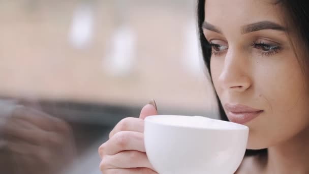 Ładna młoda dama w szlafroku pije kawę i śni przy oknie. — Wideo stockowe