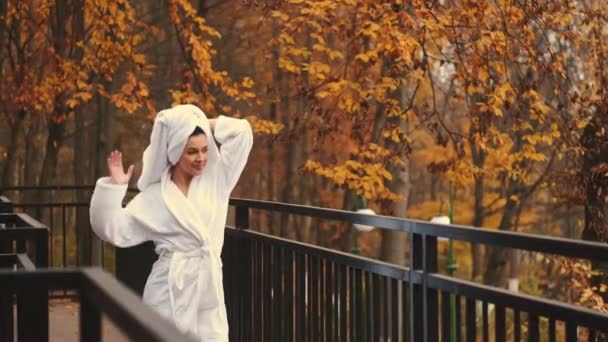 Frau im Bademantel spaziert auf der Terrasse mit schönem Blick auf den Wald im modernen Hotelzimmer — Stockvideo