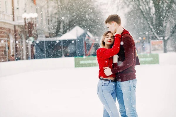 Cute para w czerwonych swetrach zabawy na arenie lodowej — Zdjęcie stockowe