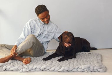 Mavi arka planda oturan yakışıklı siyah bir adam ve bir köpek.