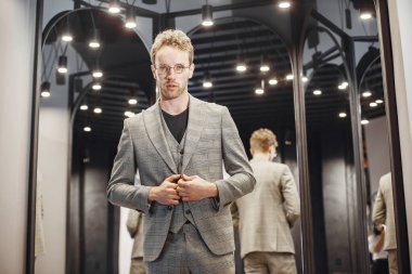 Sakallı yakışıklı bir adam dükkanda ceket seçiyor.