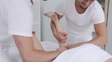 İki erkek masaj terapisti genç bir kızın bacaklarına masaj yapıyor..