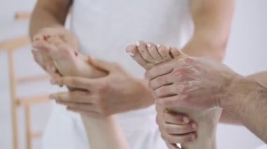 İki erkek masaj terapisti genç bir kızın bacaklarına masaj yapıyor..