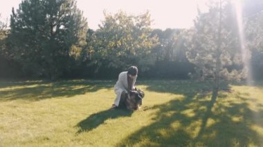 Günbatımında bahçede köpekle oynayan zarif genç bir kadın.