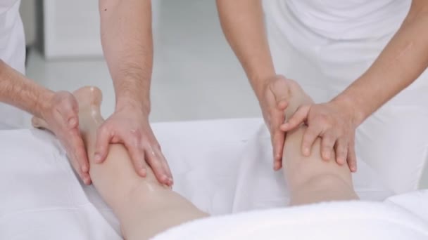 Två manliga massage terapeuter som gör massage av benen på en ung flicka. — Stockvideo