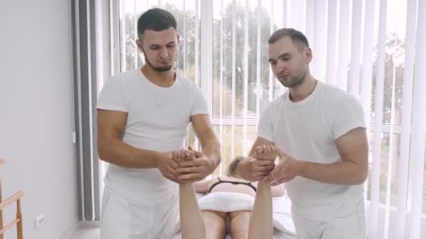 Двоє чоловіків масажистів роблять масаж ніг молодої дівчини . — стокове відео