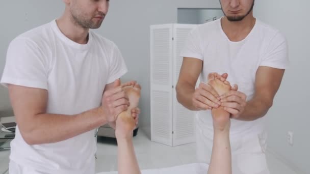Dos masajistas masculinos haciendo masaje de las piernas de una joven. — Vídeos de Stock
