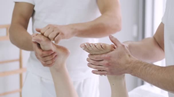 Δύο άνδρες θεραπευτές μασάζ κάνουν μασάζ στα πόδια ενός νεαρού κοριτσιού. — Αρχείο Βίντεο