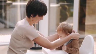 Komik oğlunu sandalyeye oturtmaya hazırlanan kadın.