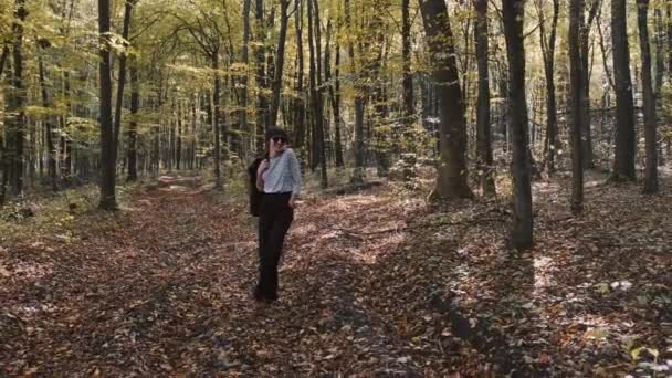 Stylowa młoda kobieta w kurtce i dżinsach spacerująca w jesiennym parku sama — Wideo stockowe