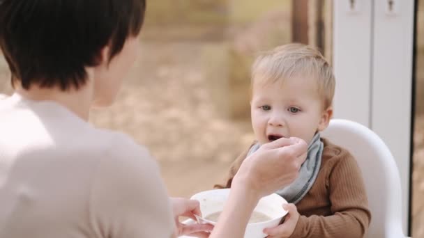 Criança sentada em uma cadeira de bebê e comendo comida com a mãe — Vídeo de Stock