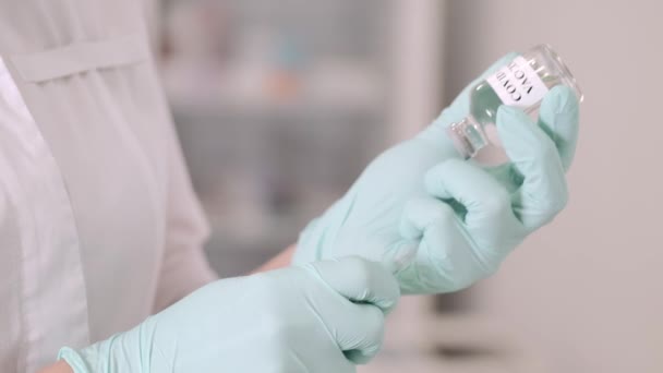 Een vrouwelijke arts in blauwe beschermende handschoenen die een medische spuit en injectieflacon vasthoudt — Stockvideo