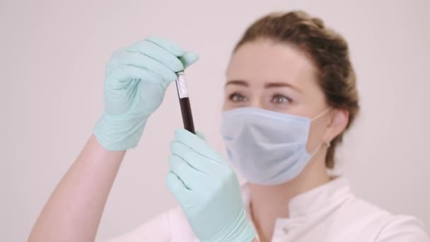 Жіночий лікар в масці дивиться на зразок крові з Коронавірусом. — стокове відео