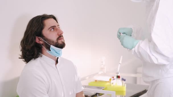Un médico con un traje de protección que toma un hisopo oral de una persona para detectar una posible infección por coronavirus — Vídeo de stock