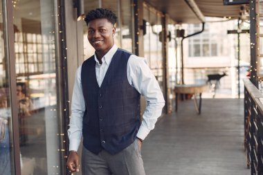 Bir kafede duran mavi gömlekli siyah adam.