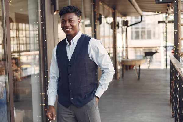 Bir kafede duran mavi gömlekli siyah adam.