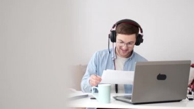 Kulaklıklı neşeli genç adam evde video konferansı yapıyor.