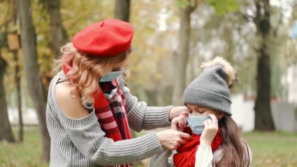 Ung mor hjälper sin dotter att sätta på sig en mask i en park — Stockvideo