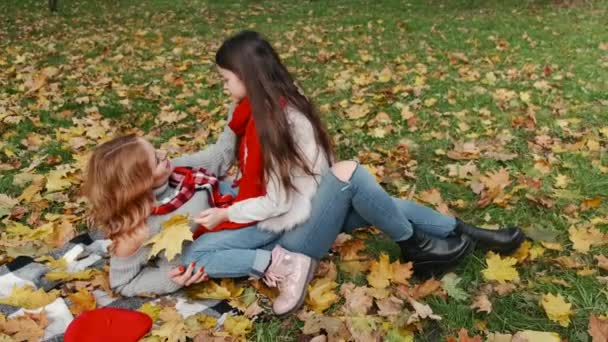 Gyönyörű anya az aranyos kislányával, juharfalevelek között fekszik az őszi parkban. — Stock videók