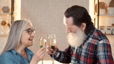 Gülümseyen yaşlı çift mutfakta şampanyayla kadeh kaldırıyor.