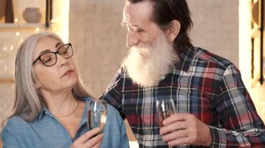 Gülümseyen yaşlı çift mutfakta şampanyayla kadeh kaldırıyor.