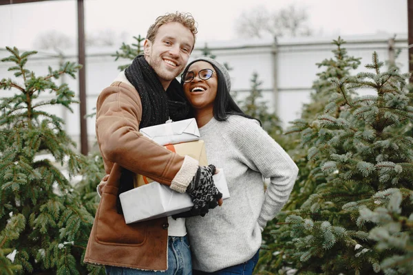 Gemischtes Paar steht mit Geschenken am Weihnachtsbaum — Stockfoto